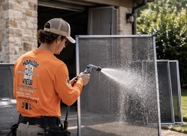 Horizon View technician in orange polo and khaki hat washing and scrubbing outdoor window mesh screens