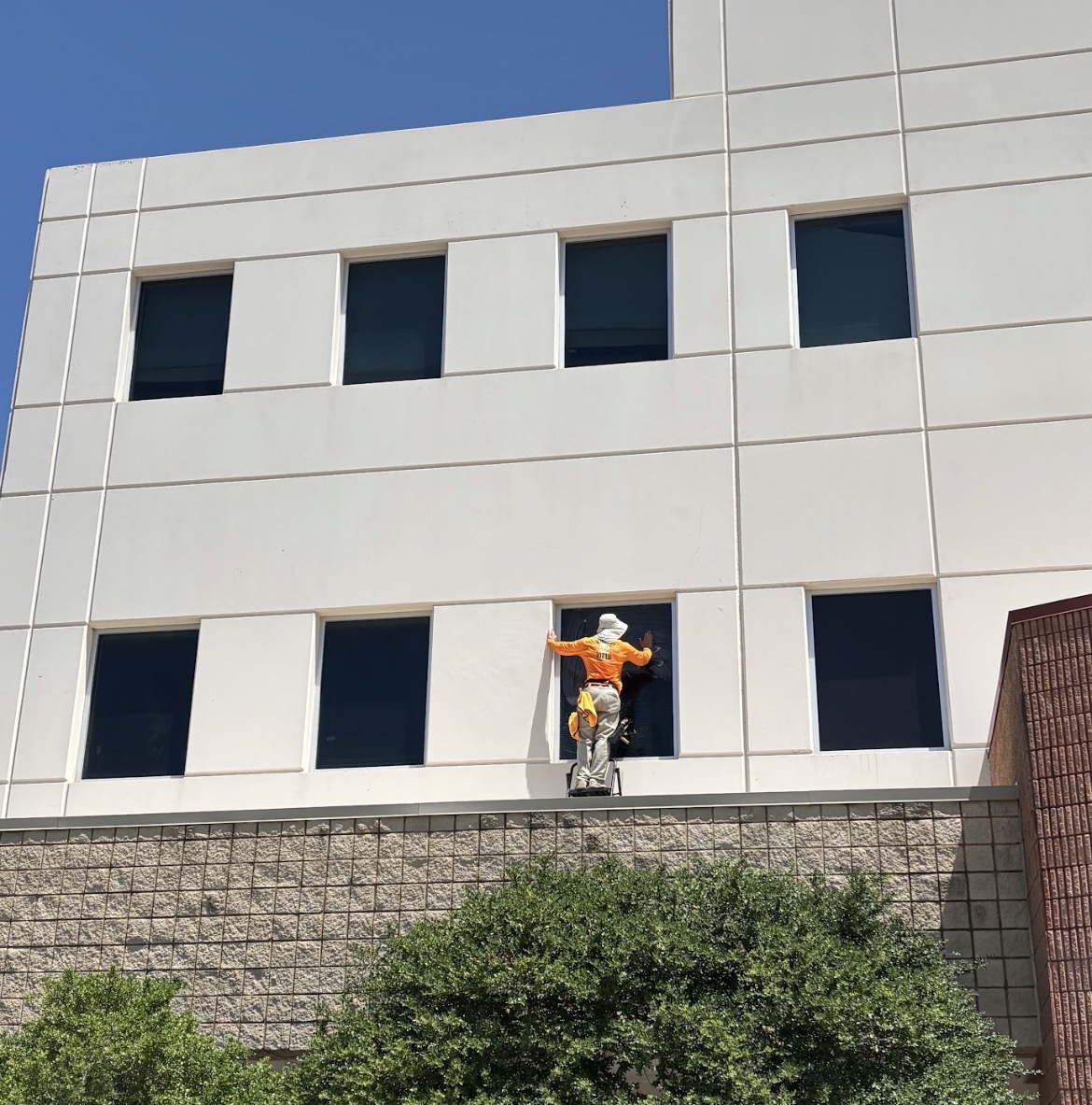 Horizon View technician in bright orange polo washing stone patio and exterior glass in Plano